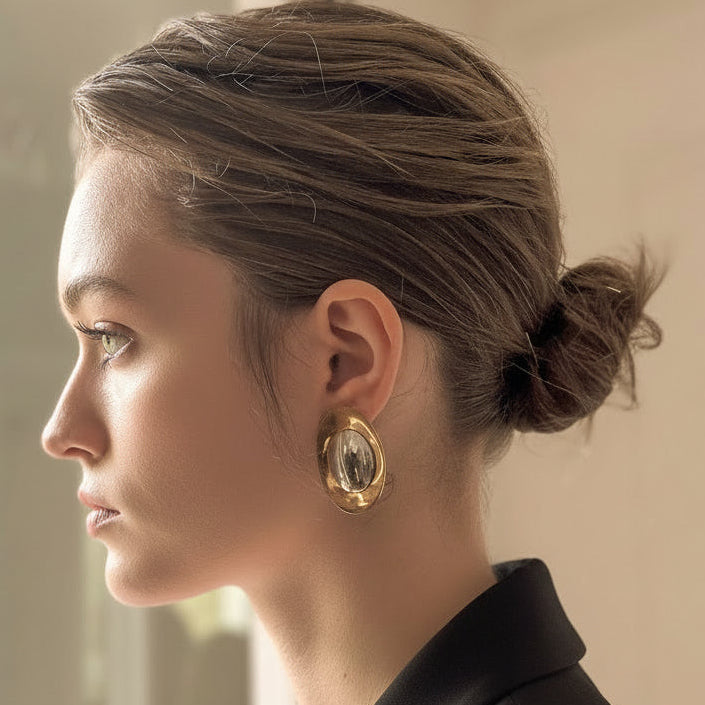 Woman with a bun hairstyle wearing gold earrings in a neutral setting