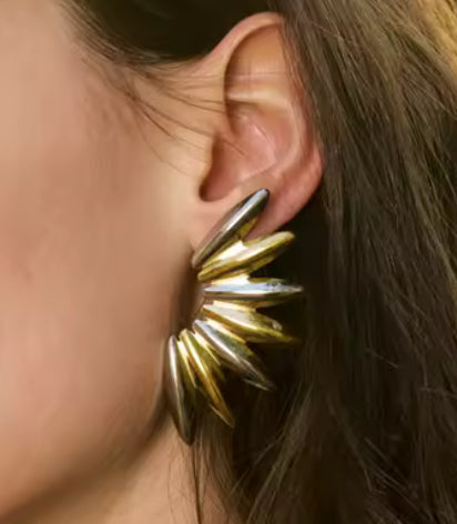 Gold spike earring worn by a person with brown hair.