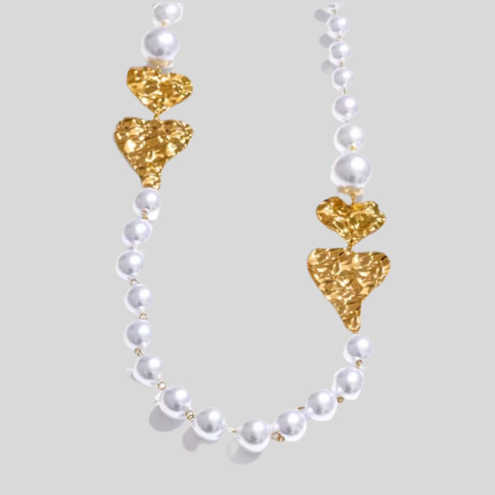 Necklace with gold heart-shaped clasps and white pearls on a light gray background
