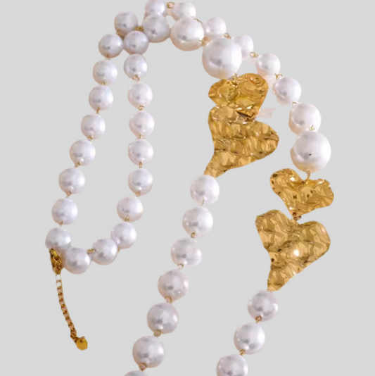 Pearl necklace with gold heart-shaped clasps on a light gray background