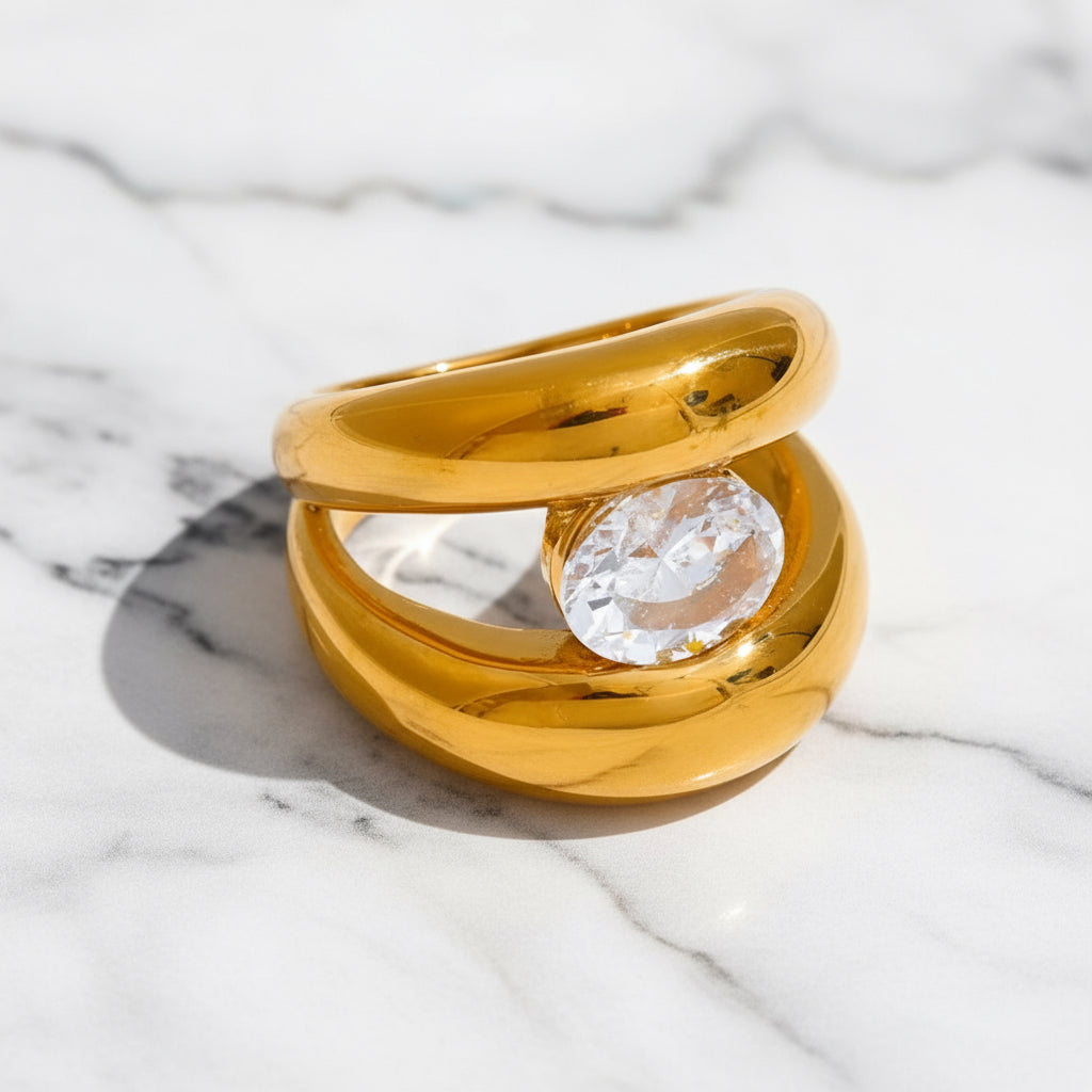 Gold ring with a clear gemstone on a marble surface