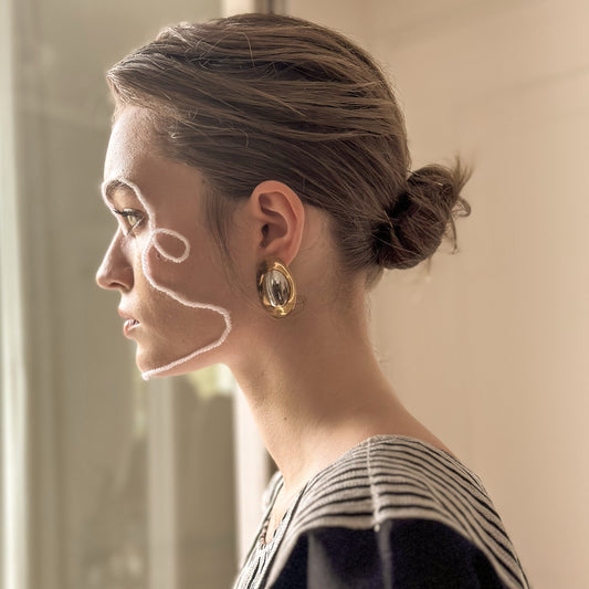 Woman with a bun hairstyle wearing gold earrings in a neutral setting