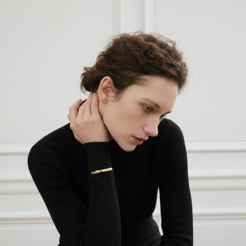 Woman in a black long-sleeve top sitting against a white wall.