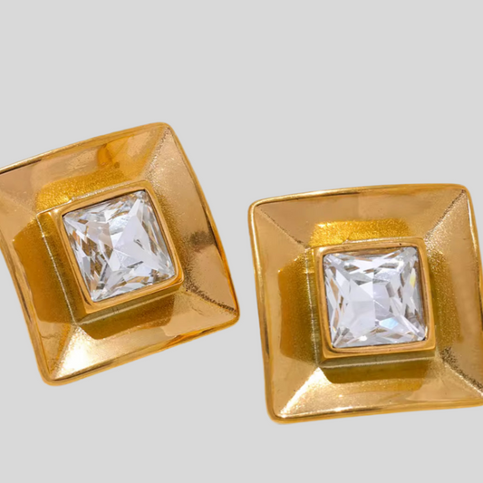 Gold square earrings with clear gemstones on a light gray background