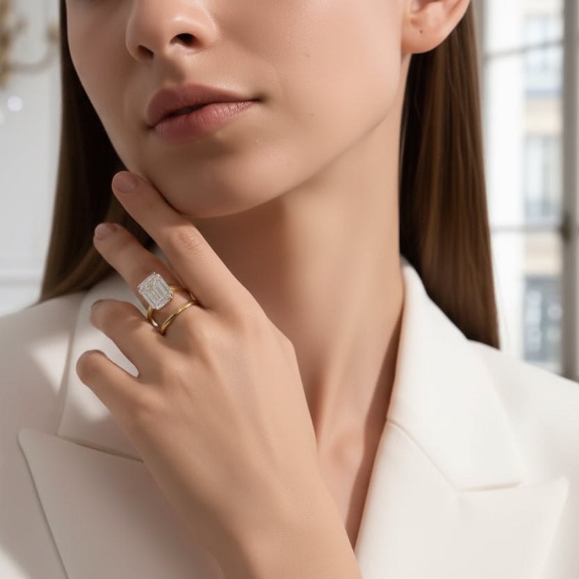 Woman wearing a white blazer with jewelry, including rings and a necklace, in a softly lit room.