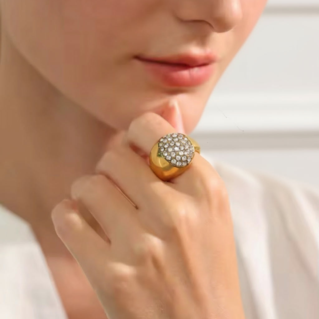 Close-up of a hand wearing a gold ring with gemstones, blurred background