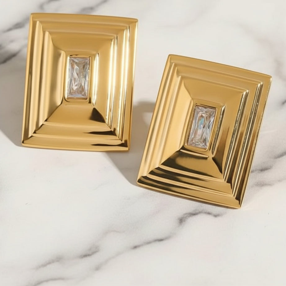 Gold earrings with rectangular design on a marble surface