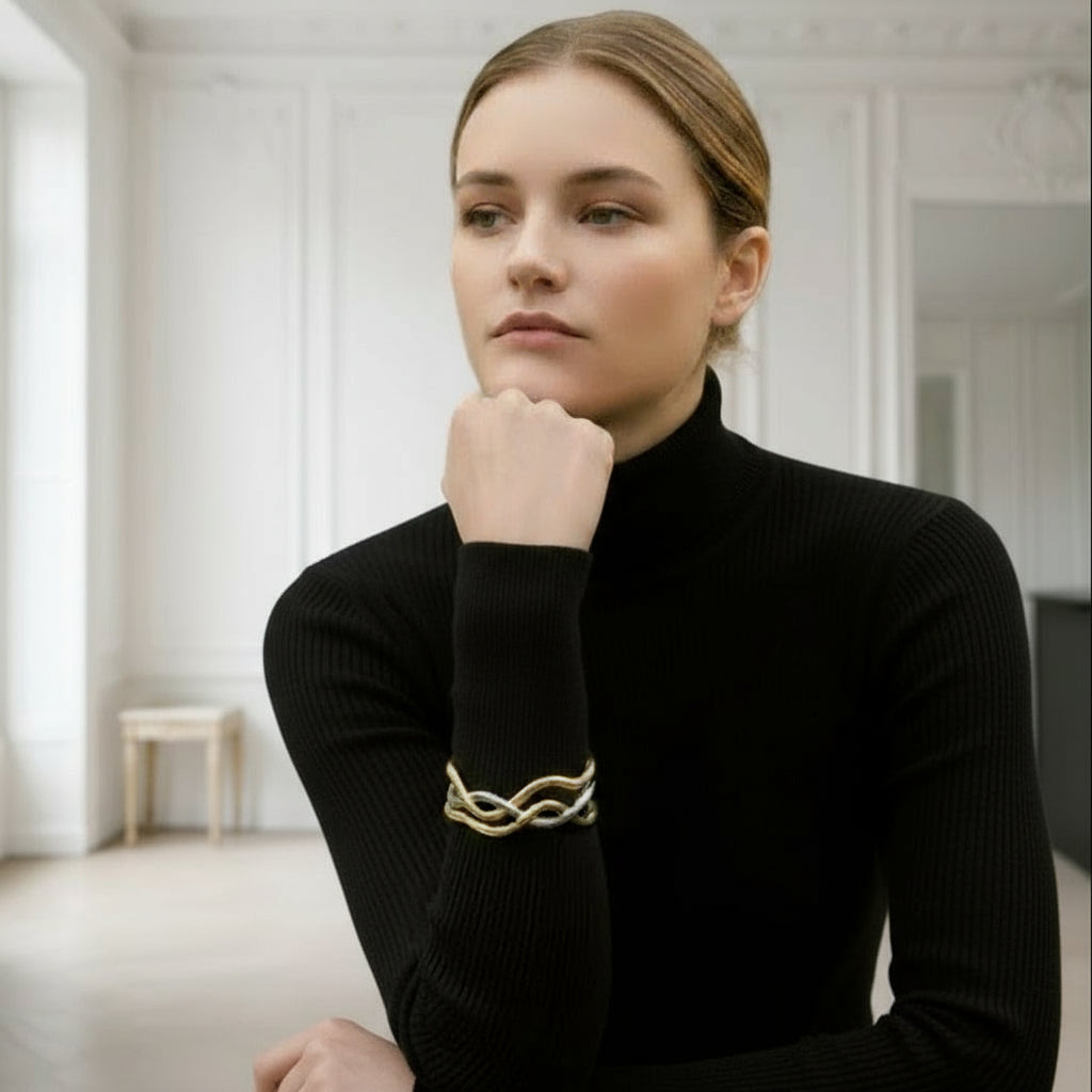 Woman wearing a gray blazer and black top with a gold bracelet on a plain background