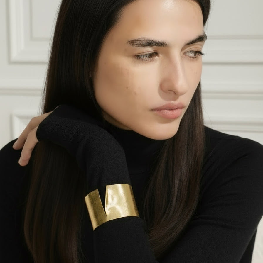 Woman wearing a black outfit with gold arm band against a white wall
