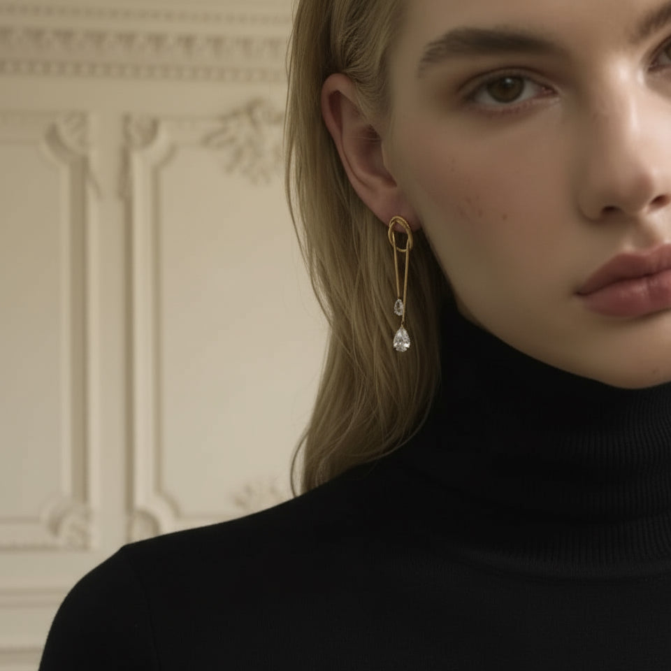 Close-up of a person wearing a gold earring with a pearl, set against a neutral background.