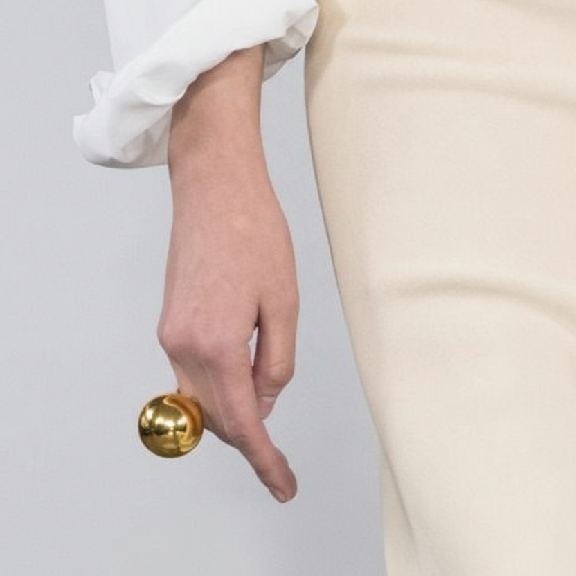 Person holding a gold doorknob against a plain background