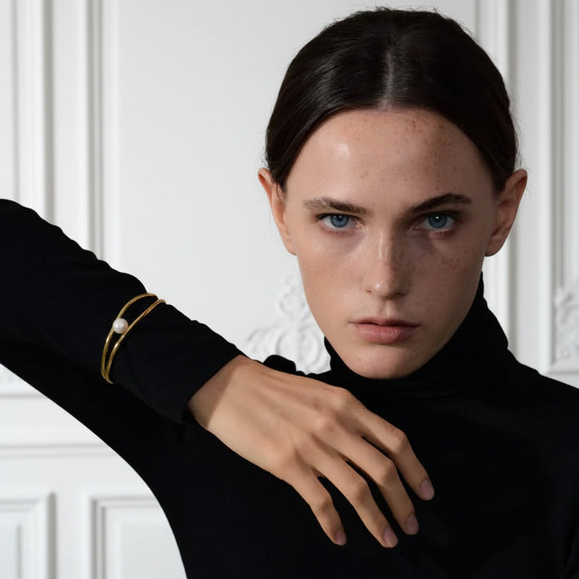 Person wearing a black turtleneck with a gold bracelet on a beige background
